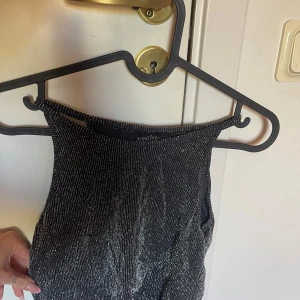 Svart glittrig klänning från XOXO Friends - Säljer en svart glittrig klänning från XOXO Friends. Klänningen har en ärmlös design med halterneck och smickrande passform. Perfekt för dig som vill sticka ut med lite extra glitter.