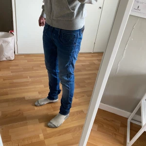 Blå Replay Anbass jeans - Säljer ett par blå Replay Anbass jeans med normal passform och klassisk femficksdesign. Jeansen har snygga slitningar och en något smalare siluett. Perfekta för dig som gillar stilrena och bekväma jeans.
