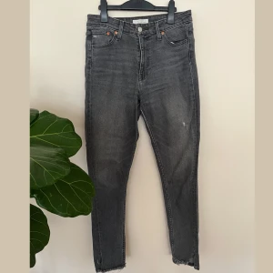 Grå Levis jeans med råa benslut - Säljer ett par grå Levis jeans med klassisk femficksdesign och råa, fransiga benslut. Jeansen har hög midja och slim fit passform, med mjuka och stretchigt denim material. Snygg tvätt och söm-detalj på baksida. 