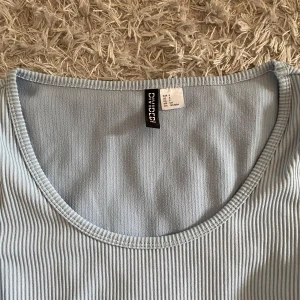 Ljusblå ribbad topp från HM - Säljer en ljusblå ribbad topp från HM. Toppen har rund halsringning och är tillverkad i ett stretchigt material som sitter snyggt på kroppen. Perfekt att matcha med jeans eller kjol.