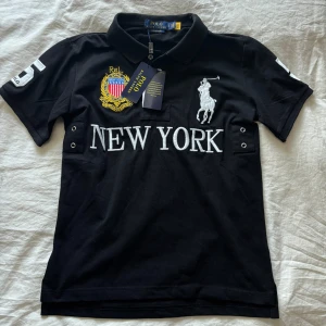 Chief keef polo🥶 - Svart pikétröja från Polo Ralph Lauren med broderad logga, stort 'NEW YORK'-tryck och siffran 5 på ryggen. Klassisk krage, korta ärmar och detaljerade broderier framtill. Slim fit-modell, perfekt för en stilren look. Den är storlek S men jag tycker att den är lite liten i storleken.