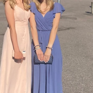 Ljusblå långklänning med volangärmar - Säljer en ljusblå långklänning med v-ringning och volangdetaljer vid ärmarna. Klänningen har omlottliv och markerad midja med knytband. Perfekt för somriga tillfällen!