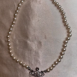 Pärlhalsband med silverfärgat Vivienne Westwood-hänge - Säljer ett  pärlhalsband från Vivienne Westwood med ett silverfärgat orb-hänge dekorerat med små stenar. Klassiska vita pärlor, säljer då det va en present från ett gammalt förhållande som jag ej vill ha kvar pris går att diskutera 