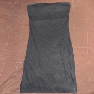 Svart kort klänning från Divided - En enkel och stilren svart klänning från Divided. Den är ärmlös och axelbandslös, perfekt att matcha med jeans eller kjol. Gjord i mjukt och stretchigt material för en bekväm passform.