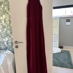 Vinröd långklänning med spetsdetaljer - Säljer en vinröd långklänning för 500kr med vackra spetsdetaljer vid axlar och rygg. Klänningen har ärmlös design och en elegant, rak passform. Perfekt för festliga tillfällen där du vill sticka ut med en stilren look. Klänningen är i superfint skick och precis som ny, endast använder under skolbalen i 9an. 