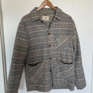 Grå rutig overshirt från Folk - Säljer en grå overshirt från Folk med rutigt mönster och tre stora fickor framtill. Jackan har knappar och klassisk krage, perfekt för lager-på-lager. Tidlös och stilren design som passar till mycket.