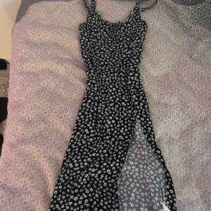 Svart blommig långklänning från Sister M - Svart långklänning med vita blommor, smala axelband och slits på sidan. Dragkedja i sidan. Fint skick! 