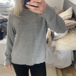 Grå stickad tröja - Mysig grå stickad tröja med rund halsringning och långa ärmar. Perfekt för kyligare dagar och enkel att matcha med olika outfits.