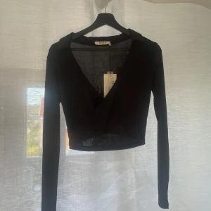 Svart omlottopp från NA-KD -  Svart omlottopp från NA-KD med lång ärm och croppad passform. Lappen är fortfarande på så inte använd alls. 