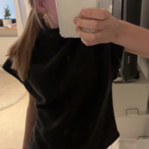 Svart t-shirt  - En klassisk svart t-shirt med rund halsringning. T-shirten har korta ärmar och en normal passform, perfekt för en enkel och stilren look.