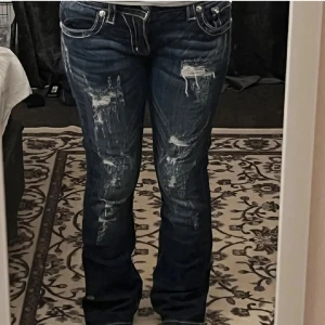 Mörkblå jeansbyxor med slitningar och broderade detaljer - Säljer ett par mörkblå jeans med tydliga slitningar framtill och broderade detaljer på bakfickorna. Storlek W29 och passar bra i längd för mig som är 166. miss me jeans