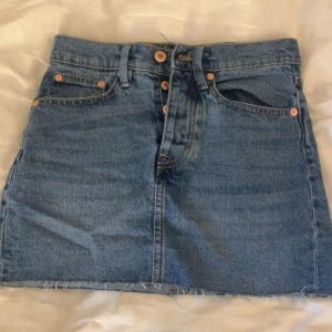 Blå jeanskjol  - Säljer en klassisk blå jeanskjol från 157 med rå kant nertill och femficksmodell. Kjolen har knappar framtill och är i en rak, kort modell, den är även highwaist. Perfekt till sommaren och enkel att matcha med olika toppar💞