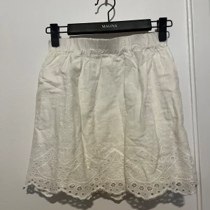 Vit broderad kjol - Supersöt vit kjol med broderade detaljer och vågig kant nertill. Kjolen har resår i midjan och är tillverkad i ett lätt linnematerial. Pris kan diskuteras🤎