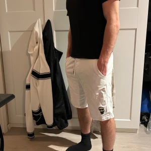 Vita shorts från Karl lagerfeldt - Snygga vita shorts med elastisk midja och snörning. På vänster ben finns ett tryck. Shortsen har sidofickor och är knälånga, perfekta för varma dagar.