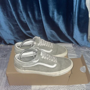 Gråa Vans/Grisch  - Säljer ett par klassiska Vans Old Skool sneakers i grå mocka med vit sula och vit sidosnöre. Skorna har snörning och den ikoniska vågformen på sidan. Perfekta för en avslappnad och stilren look.