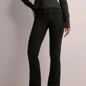 Mjuka lågmidjade kostymbyxor - Snygga svarta bootcut byxor från Nelly. Byxorna har en tight passform upptill och utsvängda ben. Prislapp sitter kvar på plagget, aldrig använda! 
