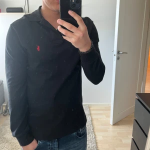Svart långärmad pikétröja från Polo Ralph Lauren - Klassisk svart långärmad pikétröja från Polo Ralph Lauren i bomull. Säljer den på grund av att den inte kommer till användning.