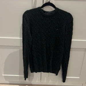 Mörkgrön kabelstickad  Morris tröja  - Snygg mörkgrön kabelstickad tröja från Morris. Klassisk rund halsringning, långärmad och med broderad logga på bröstet. Perfekt för dig som gillar stilrena och tidlösa plagg med premiumkänsla.Själv så är den för liten för mig men älskar tröjan! Nypris 1799 köpte den från NK