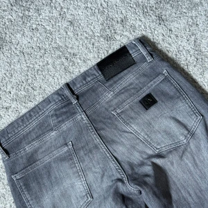 Grå Armani Jeans   - Snygga grå jeans från Armani Exchange med klassisk femficksdesign och diskret logga på bakfickan. Storlek 31x30. Jeansen har en rak passform och är tillverkade i mjukt bomullsmaterial med lite stretch för extra komfort. Perfekt för dig som gillar stilrena och moderna jeans.