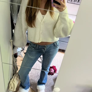 Vit croppad kofta från Gina Tricot - Superfin vit croppad kofta från Gina Tricot med ribbad struktur och stora knappar framtill. Koftan har långärmade, lite puffiga ärmar och v-ringad hals. Den är i storlek S