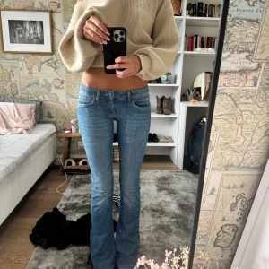 Blå bootcut jeans från Wrangler - Snygga blå jeans från Wrangler med klassisk bootcut-passform och låg midja. Jeansen har fem fickor, ljus tvätt och tydliga sömmar på bakfickorna. Materialet är slitstark denim i bomull, perfekt för dig som gillar retrovibbar och en avslappnad stil.