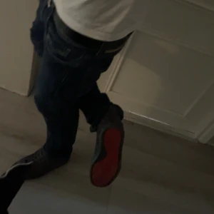 Grå Christian Louboutin sneakers - Säljer ett par grå sneakers från Christian Louboutin med den ikoniska röda sulan och signatur på undersidan. Skorna har snörning och är tillverkade i mocka, vilket ger dem en lyxig och cool vibe. Perfekta för dig som vill sticka ut med exklusiva detaljer.