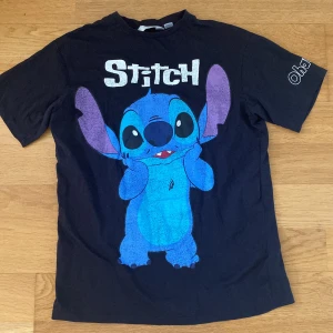 Svart oversized Stitch t-shirt från H&M  - Svart oversized t-shirt med stor färgglad Stitch-tryck på framsidan och texten 'Stitch' i vitt. På ena ärmen står det 'Ohana'. Rund hals och korta ärmar. Perfekt för dig som älskar Disney och vill ha en chill vibe.