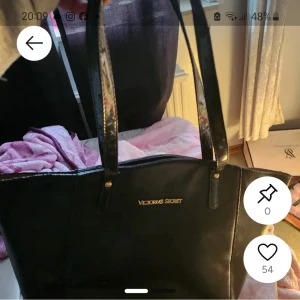 Svart axelväska från Victoria's Secret - Snygg svart axelväska från Victoria's Secret med guldigt logotyptryck framtill. Väskan har två långa handtag och är tillverkad i skinnliknande material. Perfekt storlek för att få plats med allt du behöver och passar till många olika stilar.