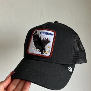 Svart keps Freedom Eagle Trucker - Svart truckerkeps från Goorin Bros med mesh på sidorna och bak.Skärmen är böjd och kepsen har justerbar passform. 