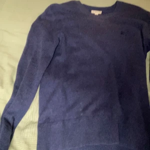 Mörkblå cashmere tröja från Burberry - Snygg mörkblå cashmere tröja från Burberry i storlek S. Tröjan har rund hals och långa ärmar, perfekt för dig som gillar klassisk stil med en lyxig touch. Materialet är mjukt och skönt, och den är enkel att matcha med jeans. Den har några defekter som på bilden med dom tre prickarna. Lite defekt. Priset kan diskuteras