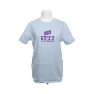 Ljusblå NOCCO t-shirt Cassis Summer - Fräsch ljusblå t-shirt från NOCCO med trycket 'Cassis Summer 2022' i lila på bröstet. Klassisk rund hals och korta ärmar. Perfekt för dig som gillar sportiga och chill vibes. Materialet är mjuk bomull som känns skönt mot huden.