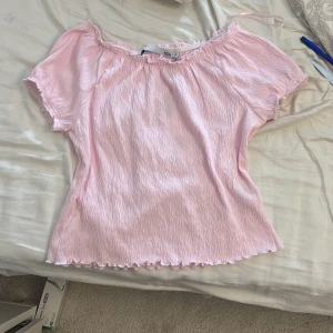 Ljusrosa offshoulder topp Maiken S - Supersöt ljusrosa topp från Maiken i storlek S. Offshoulder-modell med korta ärmar och vågig kant nertill och vid ärmslut. Materialet är lätt och krinklat, vilket ger en chill och feminin vibe. Perfekt för dig som gillar romantiska och trendiga plagg. Helt oanvänd med prislapp.