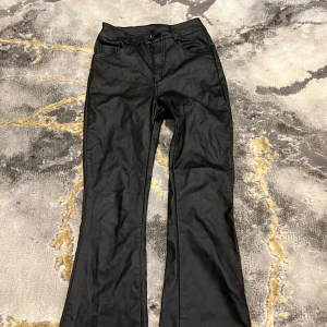 Svarta bootcut jeans med hög midja - Snygga svarta jeans med bootcut och hög midja. Klassisk femficksmodell med bälteshällor och dragkedja fram. Materialet är jeans med en lätt glansig finish som ger en cool vibe. Perfekta för dig som gillar en tidlös men trendig look.