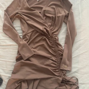 Beige omlottklänning från Chiara Forti - Säljer en beige omlottklänning från Chiara Forti med lång ärm och snygg rynkning längs sidan. Klänningen har v-ringad hals och knyt i nederkant för extra stilpoäng. Perfekt för dig som gillar trendiga detaljer och mjukt material.