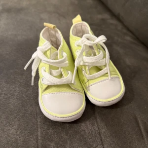 Gula babysneakers med vita detaljer - Söta babysneakers i ljusgul bomull med vita snören och tåparti. Skorna har rund tå och platt sula, perfekt för små fötter. Mjukt tyg och enkel design gör dem både bekväma och stilrena för de allra minsta.  Står ej för frakten 