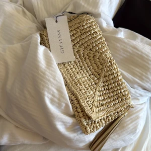 Kuvert/axel väska  från Anna field  - Snygg beige väska från Anna Field i flätad syntet med guldfärgad kedja och tofsdetalj. Väskan har magnetlås och ett innerfack, perfekt för mobilen och smågrejer. Stilren design som ger sommarkänsla och passar till många outfits.💓💓