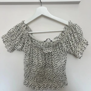 Prickig offshoulder topp Gina Tricot - Superfin offshoulder topp från Gina Tricot i vit med svarta prickar❤️ Toppen har korta puffärmar, smockad midja och volangdetaljer vid halsen. Storlek M, men passar även S/XS, hör av dig för frågor och kolla gärna in min profil för bundles ❣️❣️