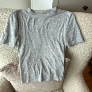 Grå ribbad t-shirt från Gina Tricot - Snygg grå ribbad t-shirt från Gina Tricot i storlek XS. T-shirten har korta ärmar, rund hals. Perfekt att styla med jeans eller kjol för en chill look. Enkel och stilren design med diskret ribbad struktur.