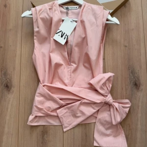 Rosa omlottopp med rosett från Zara - Supersnygg ljusrosa omlottopp från Zara med djup v-ringning och stor rosett i midjan. 