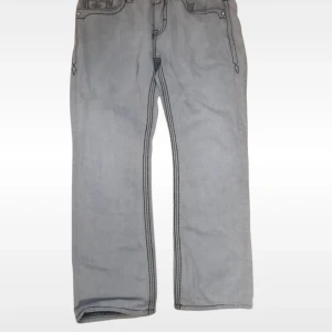 Grå jeans från Rock Revival - Snygga grå jeans från Rock Revival med coola broderade detaljer på bakfickorna och kontrastsömmar. Modellen har rak passform och klassisk femficksdesign. Materialet är 100% bomull och jeansen har en unik look som sticker ut.