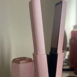 Rosa plattång med USB-laddning - Snygg plattång i ljusrosa med detaljer i roséguld. Har en mönstrad yta för bättre grepp och LED-indikatorer för värme. Kommer med USB-laddningskabel, perfekt för att styla håret snabbt och enkelt. Smidig och modern design som passar på resan eller hemma.