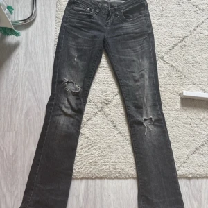 Svarta bootcut jeans från LTB - Säljer ett par svarta bootcut jeans från LTB med slitna detaljer och hål vid knäna. Jeansen har klassisk femficksdesign, låg midja och snygg tvätt med grå nyanser. Modellen är valerie
