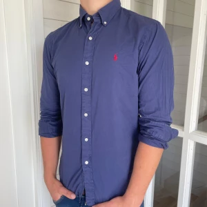 Polo Ralph lauren skjorta  - Säljer denna riktigt snygga mörkblåa Ralph lauren skjorta, den är i bra skick bara lite solblekt men annars bra skick, den är i storlek M och modell slim fit, den är 70 cm lång och 49 cm bred under armhålorna, hör gärna av dig vid frågor 