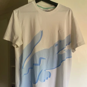 Vit t-shirt med blå krokodil från Lacoste - Väldigt bra sick Knappast använd. Ny pris 1000kr. Skriv vid någon fråga ! 