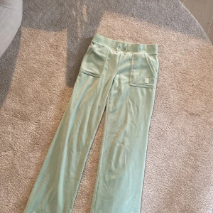 Mintgröna Juicy Couture XS - Snygga mintgröna mjukisbyxor från Juicy Couture i storlek XS. Byxorna har bred resår i midjan med snörning, stora fickor med lock och silverfärgade knappar framtill samt broderad JC-logga. Mjukt material som känns lyxigt och chill.                                                    (Har en liten fläck på baksidan).