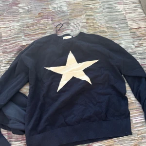 Mörkblå stickad tröja med stjärna - Snygg mörkblå stickad tröja från Stella Nova med en stor vit stjärna på bröstet. Tröjan har rund hals och långa ärmar, perfekt för dig som gillar enkel men cool design. Materialet är mjukt och skönt, passar till jeans eller kjol. ALDRIG ANVÄND