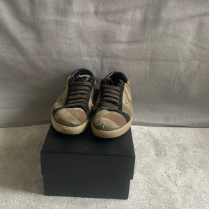 Saint Laurent camo sneakers - Snygga sneakers från Saint Laurent med camouflagemönster i grönt, brunt och beige. Skorna har svarta snören, rund tå och platt sula. Utsidan är i textil och mocka, med Saint Laurent-logga på sidan. Perfekt för dig som gillar streetstyle och designer.allt og där framme är dom största defekten