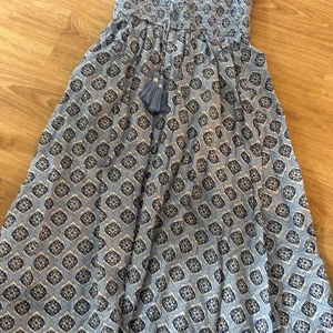 Blå långklänning från Gina Tricot - Säljer en blå långklänning från Gina Tricot med snyggt mönster i mörkblått och vitt. Klänningen har smock upptill och ett boho-inspirerat print över hela tyget. Den har en avslappnad passform och dekorativa tofsar framtill. Perfekt för sommarens alla tillfällen!