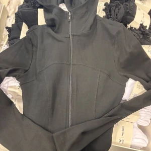 Svart zip hoodie jacka Gina Tricot - Svart hoodiejacka från Gina Tricot med hel dragkedja framtill och huva. Jackan har en clean look med markerade sömmar och lång ärm. Perfekt för chill dagar eller när du vill ha en enkel streetstyle. Materialet är mjukt och känns skönt mot huden.