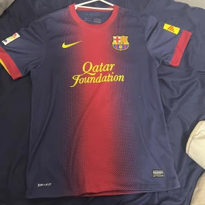 FC Barcelona matchtröja Nike Dri-Fit - Säljer en FC Barcelona matchtröja från Nike med Dri-Fit material. Tröjan är marinblå med röd mitt och gula detaljer, har korta ärmar och rund hals. Framsidan har Qatar Foundation-tryck och klubbmärke, baksidan har UNICEF-tryck. Snyggt prickigt mönster över bröstet.